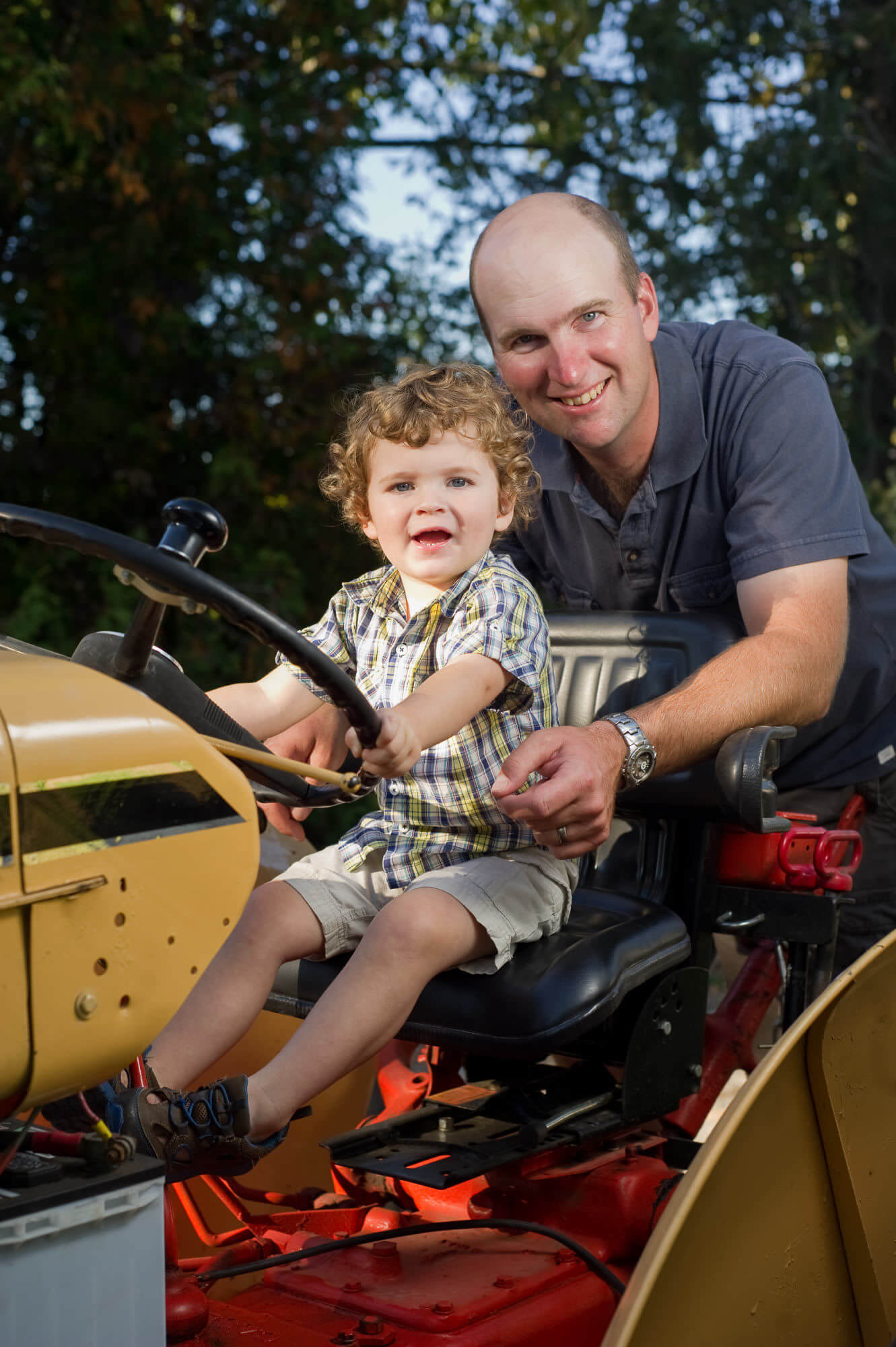 Family portrait of young boy with father sitting on a vintage tractor by Nick Perry Photography