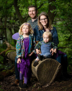 Family of four including two young children posting for a photo in a forest