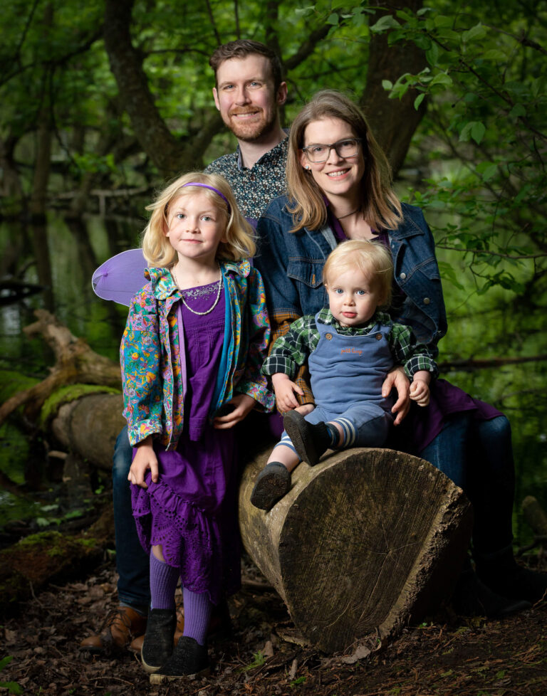 Family of four including two young children posting for a photo in a forest
